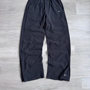 Puede incluir: Pantalones deportivos negros con un logotipo blanco de Nike en la parte delantera y cerca del tobillo. Los pantalones tienen cintura el&aacute;stica y bolsillos laterales. Las piernas tienen cremalleras en la parte inferior. Los pantalones son de material ligero.