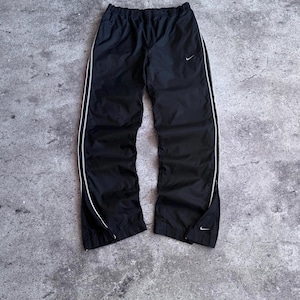 Puede incluir: Pantalón de chándal Nike negro con cintura elástica, un pequeño logotipo swoosh blanco en el muslo izquierdo y un fino ribete blanco a lo largo de cada pierna. Los bajos de las perneras incluyen cremalleras y un pequeño logotipo swoosh.