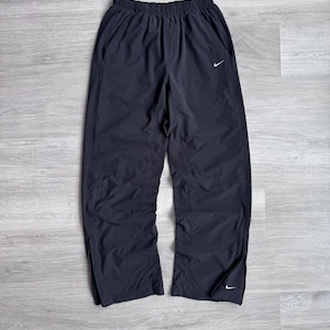 Puede incluir: Pantalones de ch&aacute;ndal Nike negros con cintura el&aacute;stica y bolsillos laterales. Los pantalones presentan un peque&ntilde;o logotipo blanco de Nike en la pierna izquierda y cremalleras en los tobillos. Fabricados con un material ligero.