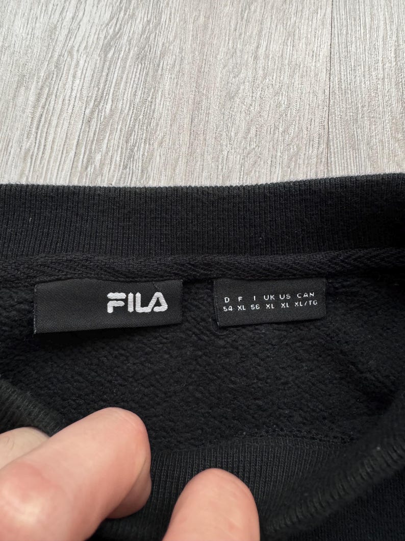 Peut inclure: Sweat-shirt noir &agrave; col rond avec une &eacute;tiquette FILA. L'&eacute;tiquette comprend des informations de taille : D 54, F XL, I XL, UK XL, US XL, CAN XL/TG.
