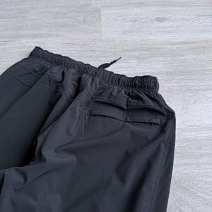 Puede incluir: Pantalones deportivos negros con cintura el&aacute;stica y cord&oacute;n. Los pantalones tienen un bolsillo trasero y un ajuste relajado. La tela parece ser un material ligero y transpirable, adecuado para entrenamientos o ropa casual.
