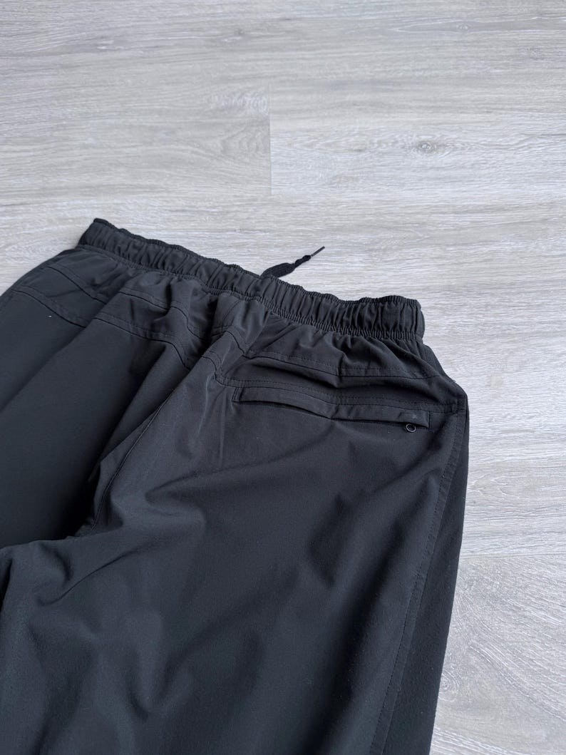 Puede incluir: Pantalones deportivos negros con cintura el&aacute;stica y cord&oacute;n. Los pantalones tienen un bolsillo trasero y un ajuste relajado. La tela parece ser un material ligero y transpirable, adecuado para entrenamientos o ropa casual.