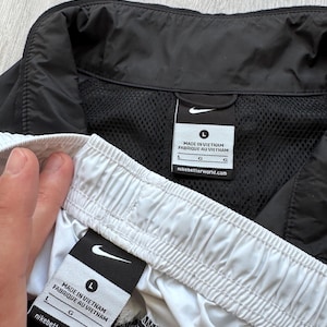 Peut inclure: Shorts et veste de sport noirs et blancs. Le short a une taille blanche et la veste a une doublure en mesh noire. Les deux articles portent le logo Nike et des &eacute;tiquettes indiquant "Made in Vietnam".