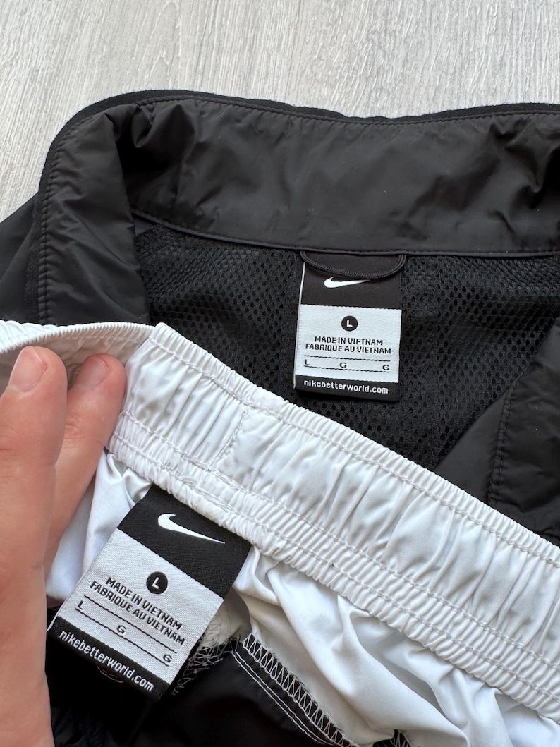 Peut inclure: Shorts et veste de sport noirs et blancs. Le short a une taille blanche et la veste a une doublure en mesh noire. Les deux articles portent le logo Nike et des &eacute;tiquettes indiquant "Made in Vietnam".