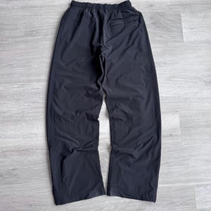 Puede incluir: Pantalones deportivos negros con cintura el&aacute;stica y un bolsillo trasero. Los pantalones est&aacute;n hechos de un material ligero y ligeramente brillante. Las perneras son rectas y anchas.