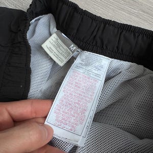 Puede incluir: Pantalones cortos deportivos negros con forro de malla blanco. Los pantalones cortos tienen una cintura con cord&oacute;n y una etiqueta con instrucciones de cuidado. La etiqueta dice "Made in Malaysia".