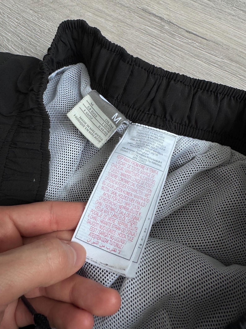 Puede incluir: Pantalones cortos deportivos negros con forro de malla blanco. Los pantalones cortos tienen una cintura con cord&oacute;n y una etiqueta con instrucciones de cuidado. La etiqueta dice "Made in Malaysia".