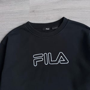 Peut inclure: Sweat-shirt noir &agrave; col rond avec le logo FILA blanc sur la poitrine. Le logo est soulign&eacute; en blanc. Le sweat-shirt a un design simple et classique, adapt&eacute; aux tenues d&eacute;contract&eacute;es.