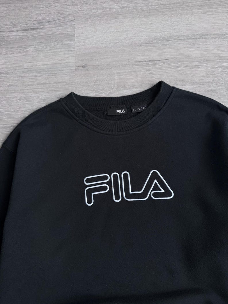 Peut inclure: Sweat-shirt noir &agrave; col rond avec le logo FILA blanc sur la poitrine. Le logo est soulign&eacute; en blanc. Le sweat-shirt a un design simple et classique, adapt&eacute; aux tenues d&eacute;contract&eacute;es.