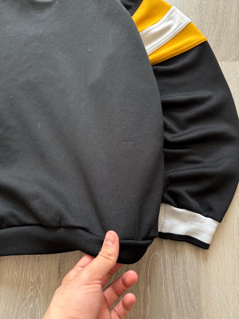 Puede incluir: Sudadera negra con rayas amarillas y blancas en la parte superior de la manga. El pu&ntilde;o es blanco con una raya negra. El dobladillo inferior es negro. La tela parece ser un material suave y c&oacute;modo.