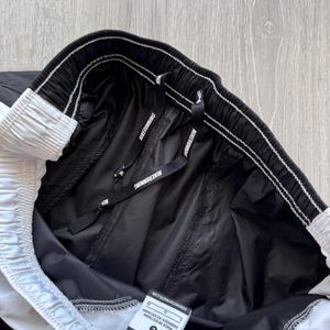 Peut inclure: Short de course Nike noir et blanc. Le short a une taille &eacute;lastique avec le texte "NIKE RUNNING" sur le cordon de serrage. Le short a une bande blanche sur le c&ocirc;t&eacute; et une &eacute;tiquette indiquant "MADE IN VIETNAM".