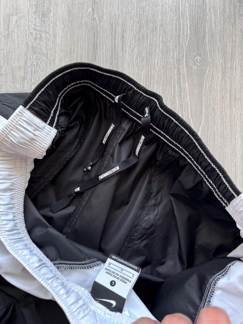 Peut inclure: Short de course Nike noir et blanc. Le short a une taille &eacute;lastique avec le texte "NIKE RUNNING" sur le cordon de serrage. Le short a une bande blanche sur le c&ocirc;t&eacute; et une &eacute;tiquette indiquant "MADE IN VIETNAM".