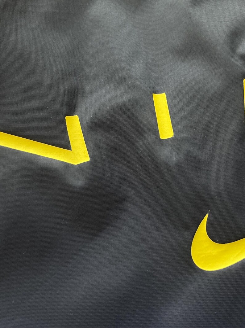 May include: A dark gray fabric with yellow cut-out shapes, including a curved checkmark and several straight lines. The shapes are arranged in a scattered pattern across the surface.