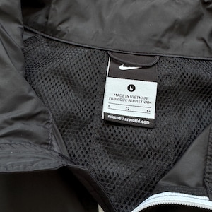 Peut inclure: Veste noire avec une doublure en mesh et une fermeture &eacute;clair blanche. La veste porte le logo Nike et une &eacute;tiquette indiquant "MADE IN VIETNAM FABRIQUE AU VIETNAM" et "nikebetterworld.com". La veste est de taille L.