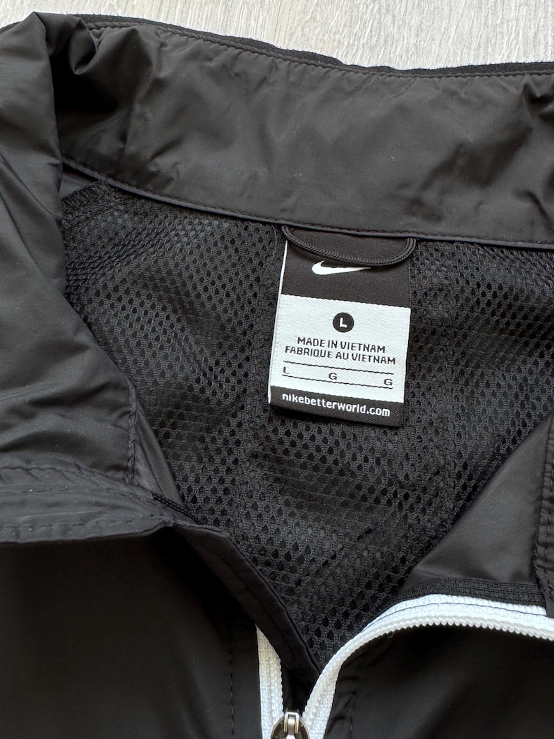 Peut inclure: Veste noire avec une doublure en mesh et une fermeture &eacute;clair blanche. La veste porte le logo Nike et une &eacute;tiquette indiquant "MADE IN VIETNAM FABRIQUE AU VIETNAM" et "nikebetterworld.com". La veste est de taille L.