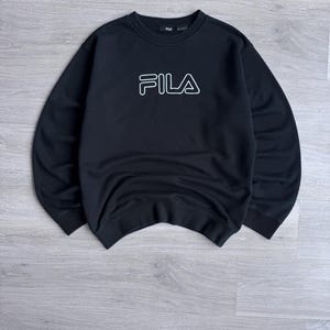 Peut inclure: Sweat-shirt noir &agrave; col rond avec le logo FILA blanc soulign&eacute; sur la poitrine. Le sweat-shirt est fait d'une mati&egrave;re douce et a un style classique et d&eacute;contract&eacute;. Le logo FILA est centr&eacute; sur le devant.