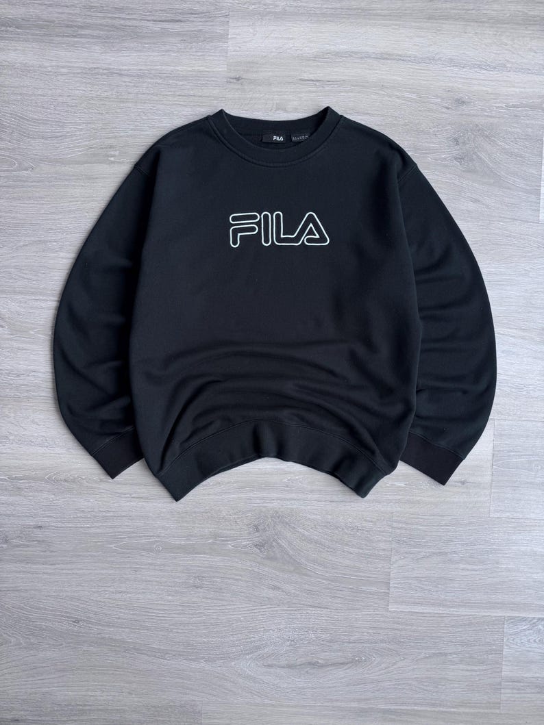 Peut inclure: Sweat-shirt noir &agrave; col rond avec le logo FILA blanc soulign&eacute; sur la poitrine. Le sweat-shirt est fait d'une mati&egrave;re douce et a un style classique et d&eacute;contract&eacute;. Le logo FILA est centr&eacute; sur le devant.