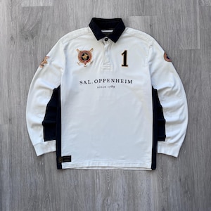 May include: White long-sleeve polo shirt with black accents and a black collar. The shirt features the text "SAL. OPPENHEIM" and "since 1789" in black, along with the number "1" and a crest on the chest. The sleeves have patches.