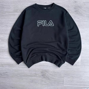 Peut inclure: Sweat-shirt noir avec le logo FILA blanc sur la poitrine. Le sweat-shirt &agrave; col rond a des manches longues. Le logo est soulign&eacute; en blanc. Le v&ecirc;tement est fait d'une mati&egrave;re douce.