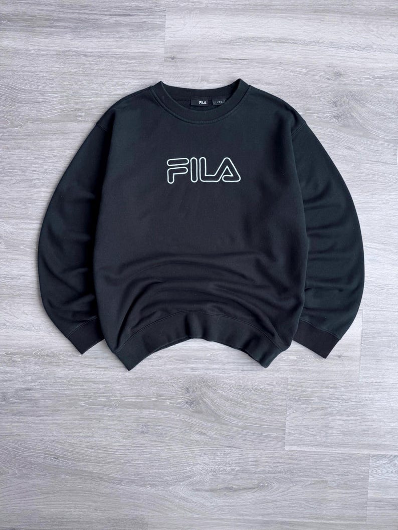 Peut inclure: Sweat-shirt noir avec le logo FILA blanc sur la poitrine. Le sweat-shirt &agrave; col rond a des manches longues. Le logo est soulign&eacute; en blanc. Le v&ecirc;tement est fait d'une mati&egrave;re douce.