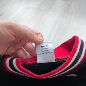 May include: Black sweatshirt with a red and white striped collar. The tag shows the Nike logo and the text "RN#56323 CA#05553 RFC# NME 920220 KL4".