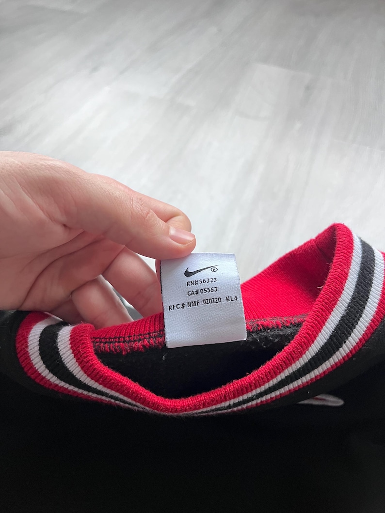 May include: Black sweatshirt with a red and white striped collar. The tag shows the Nike logo and the text "RN#56323 CA#05553 RFC# NME 920220 KL4".