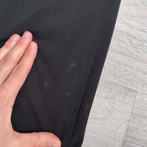 Puede incluir: Primer plano de tela negra con una costura visible en el lado derecho. La tela tiene varias manchas peque&ntilde;as de color claro. La imagen est&aacute; tomada en &aacute;ngulo, mostrando una parte del material.