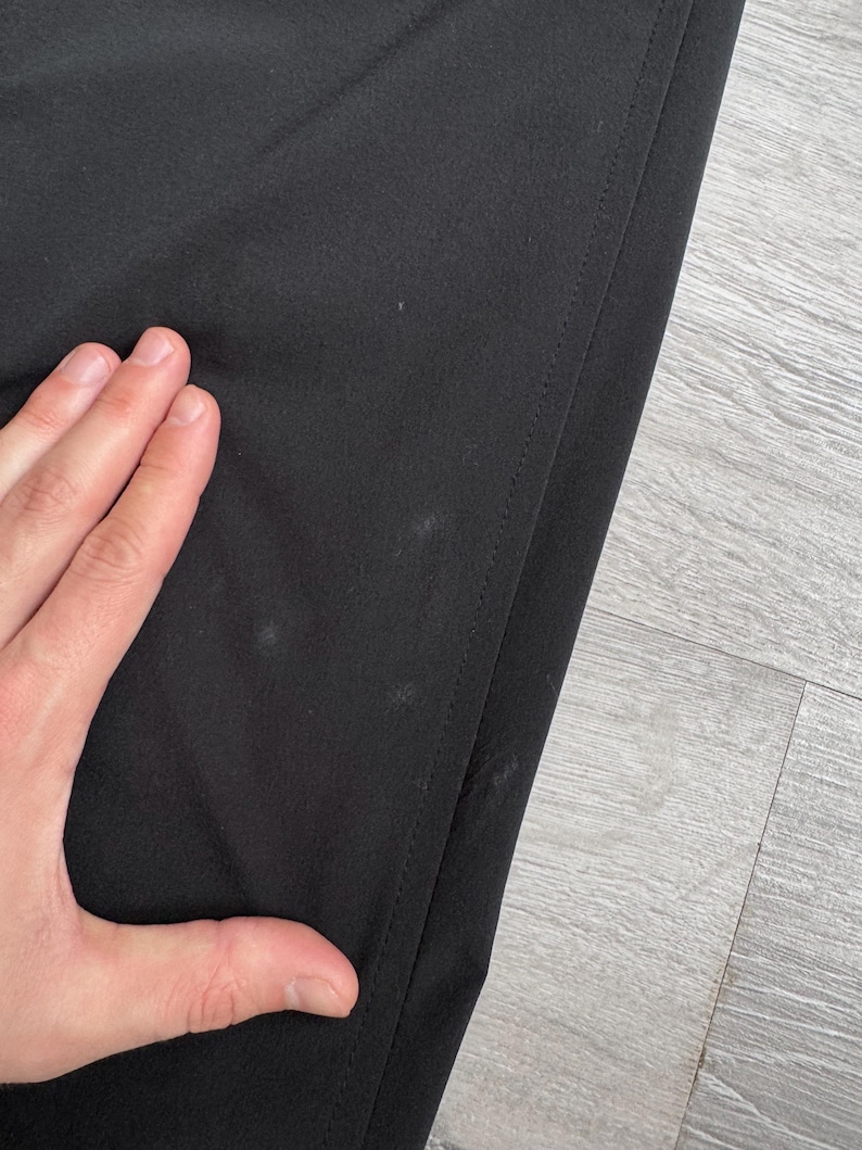 Puede incluir: Primer plano de tela negra con una costura visible en el lado derecho. La tela tiene varias manchas peque&ntilde;as de color claro. La imagen est&aacute; tomada en &aacute;ngulo, mostrando una parte del material.