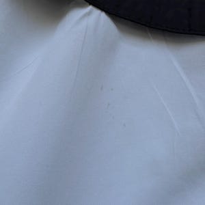 Peut inclure: Gros plan sur un tissu bleu clair avec une bordure noire en haut. Le tissu a une texture lisse et quelques petites taches. La bordure noire est incurv&eacute;e, possiblement une partie d'un v&ecirc;tement.