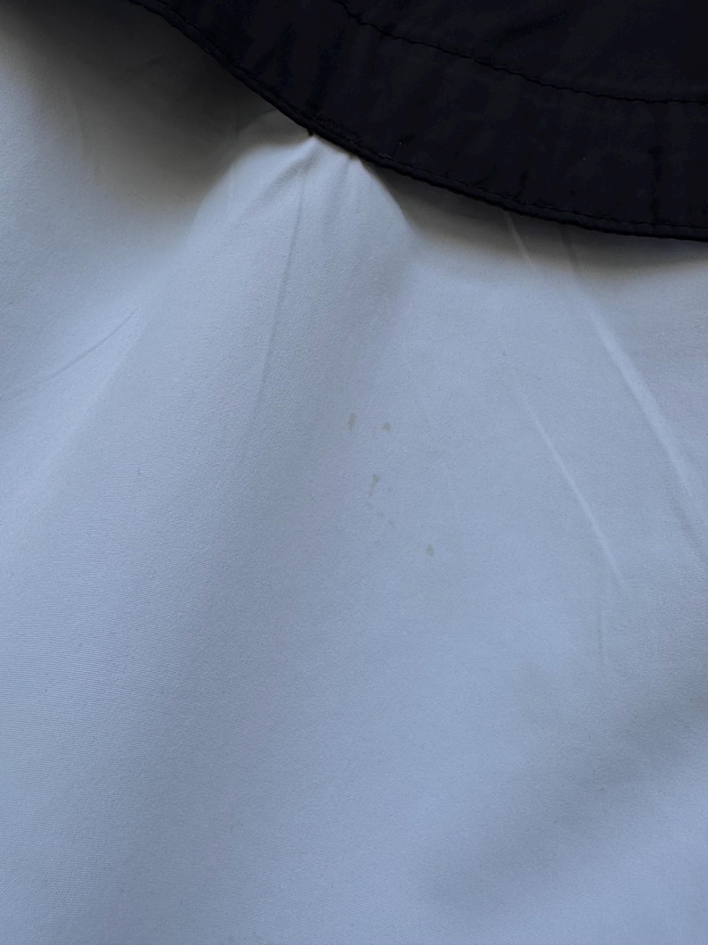 Peut inclure: Gros plan sur un tissu bleu clair avec une bordure noire en haut. Le tissu a une texture lisse et quelques petites taches. La bordure noire est incurv&eacute;e, possiblement une partie d'un v&ecirc;tement.