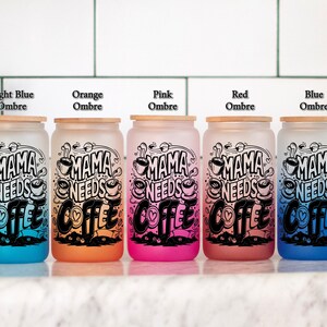 May include: Five frosted glass canisters with bamboo lids in ombre colors of light blue, orange, pink, red, and blue. Each canister has a black and white graphic that says "Mama Needs Coffee" with a heart and coffee cup design.