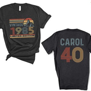 May include: Two black t-shirts. One shirt has a vintage design with the text "Vintage Est. 1985 Limited Edition". The other shirt has the text "Carol 40" in a retro style.