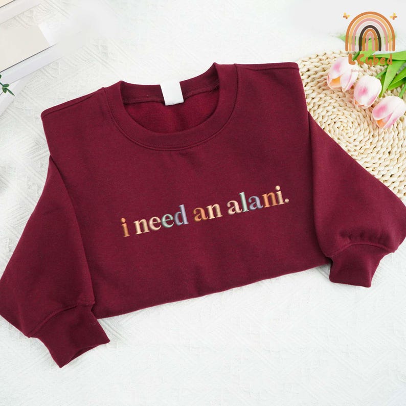 May include: Burgundy sweatshirt with the text "i need an alani." in rainbow colors.