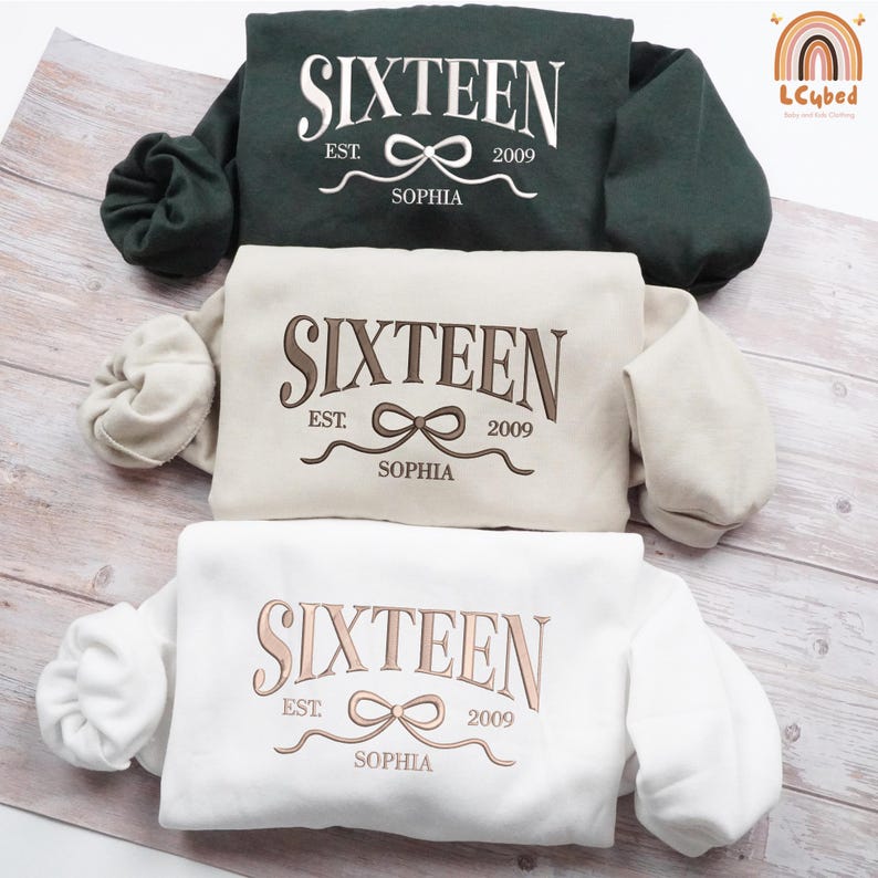 May include: Three sweatshirts in dark green, beige, and white, each embroidered with the word "SIXTEEN", the year "2009", and the name "SOPHIA". The design includes a bow and the word "EST."