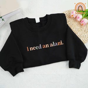 May include: Black sweatshirt with the text "i need an alani." in rainbow colors.