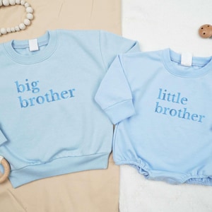 May include: Two light blue baby onesies with embroidered text. The larger onesie says "big brother" and the smaller onesie says "little brother".