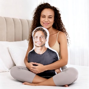 May include: A custom-shaped throw pillow featuring a photographic print of a smiling person with brown hair wearing a dark gray t-shirt. The pillow is die-cut to follow the outline of the person's head and torso, creating a realistic portrait cushion.