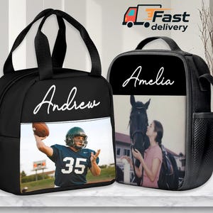 Op de afbeelding: Twee zwarte lunchtassen met witte scriptnamen. Eén tas heeft een American footballspeler met de naam "Andrew". De andere tas heeft een foto van een persoon met een paard en de naam "Amelia". Beide tassen hebben zwarte handvatten.