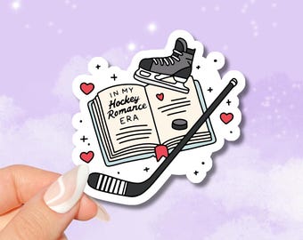 Może przedstawiać: Naklejka przedstawiająca książkę z tekstem "In My Hockey Romance Era" oraz kij hokejowy, krążek i łyżwę. Książka i kij są ozdobione sercami.