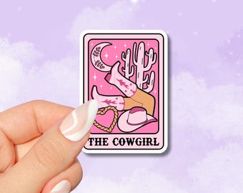 Op de afbeelding: Roze en witte sticker met een cartoonillustratie van een cowgirl die cowboylaarzen en een cowboyhoed draagt. De cowgirl ligt met haar benen in de lucht. De sticker heeft een roze achtergrond met een halve maan, sterren en een cactus. De tekst "THE COWGIRL" staat onderaan de sticker gedrukt.