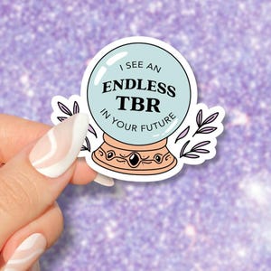 Könnte beinhalten: Ein Aufkleber mit einer blauen Kristallkugel mit dem Text "I see an endless TBR in your future". Die Kristallkugel steht auf einem Sockel mit einer goldenen Basis und einem schwarzen Edelstein.