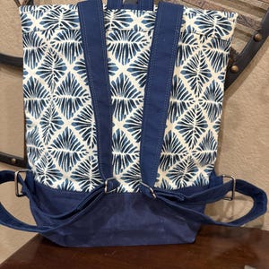 May include: A blue and white patterned backpack with adjustable straps and a navy blue base. The backpack has a flap closure and a top handle.
