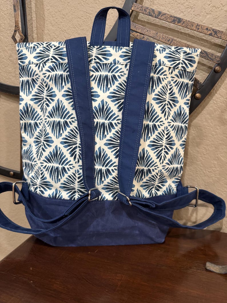 May include: A blue and white patterned backpack with adjustable straps and a navy blue base. The backpack has a flap closure and a top handle.