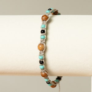 May include: A beige macrame bracelet with turquoise, brown, and black beads.