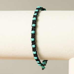 May include: A black and turquoise beaded bracelet. The bracelet is made with small turquoise beads and black cord.