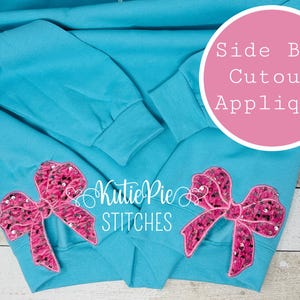 May include: A turquoise sweatshirt with two pink sequined bow appliques on the sleeves. The bows have a dark pink and black pattern. The text "Side Bow Cutout Applique" is in a pink circle. The text "Kutie Pie STITCHES" is also visible.