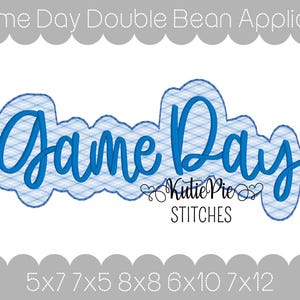 May include: A blue and white applique design with the words "Game Day" in a script font. The text is outlined in blue and filled with a plaid pattern. The design includes the text "Kutie Pie STITCHES".