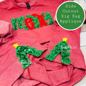 Peut inclure: Sweat-shirt rouge avec le mot "merry" en sequins verts et rouges. Le sweat-shirt a deux appliques de sapin de Noël en sequins verts sur les manches. Le texte "Side Cutout Zig Zag Applique" est écrit en vert sur fond blanc.