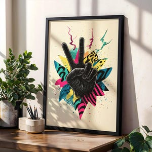 May include: Black framed art print featuring a black hand making the peace sign. The hand is set against a colorful background of yellow, pink, blue, and green shapes. The artwork has a retro, pop art style.