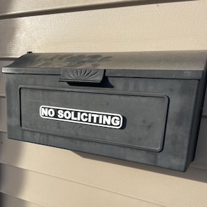 May include: A black mailbox with a white sign that reads "NO SOLICITING".
